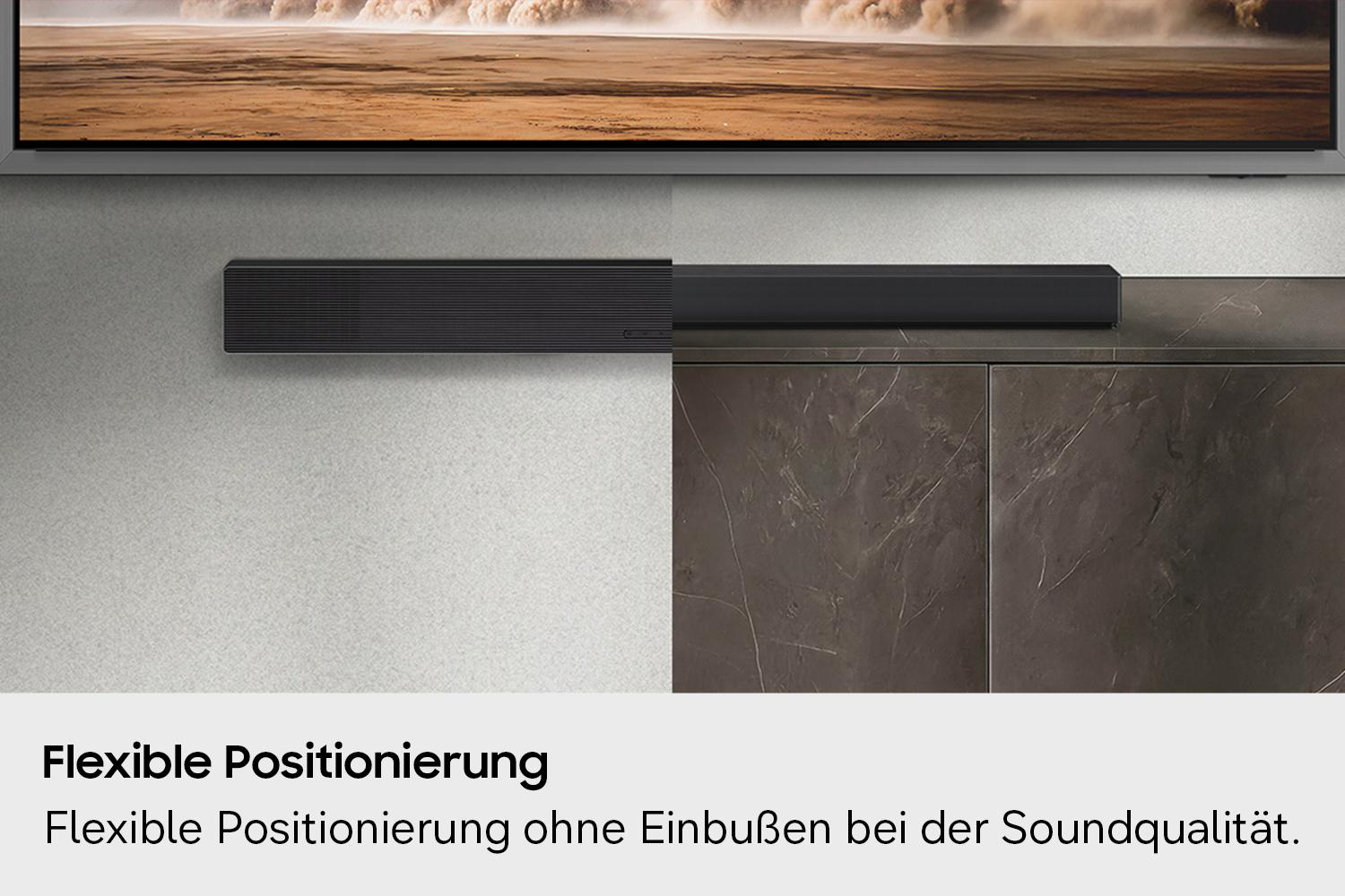 Schwarzer Soundbar vor einem Fernseher und dunklen Schrankfronten.