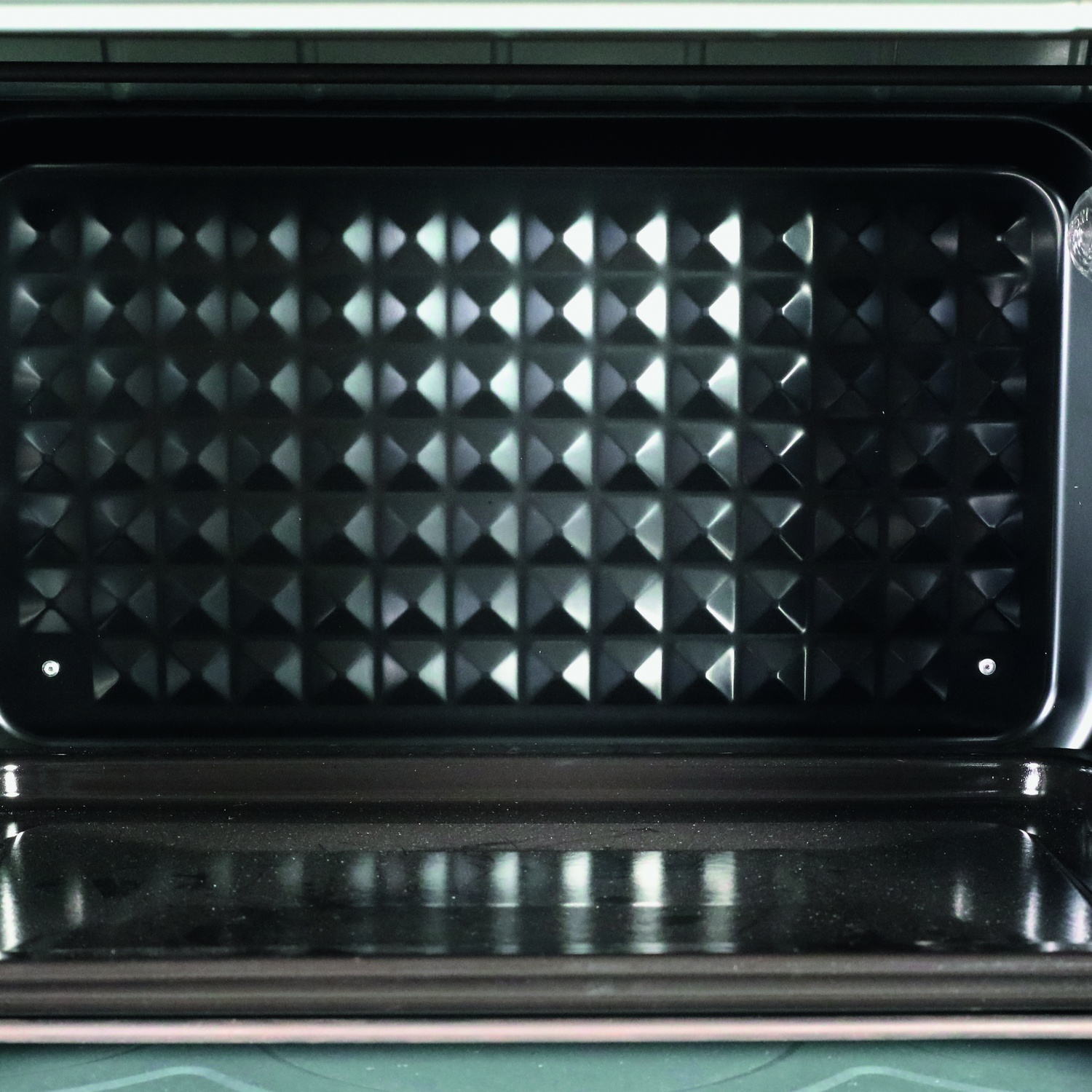Vista interna di un forno pulito con teglia texturizzata e cassetto inferiore.