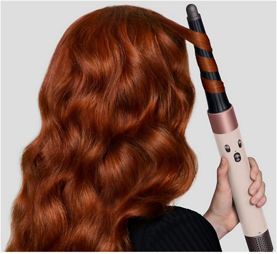Une personne aux longs cheveux roux coiffe une mèche avec un fer à friser.