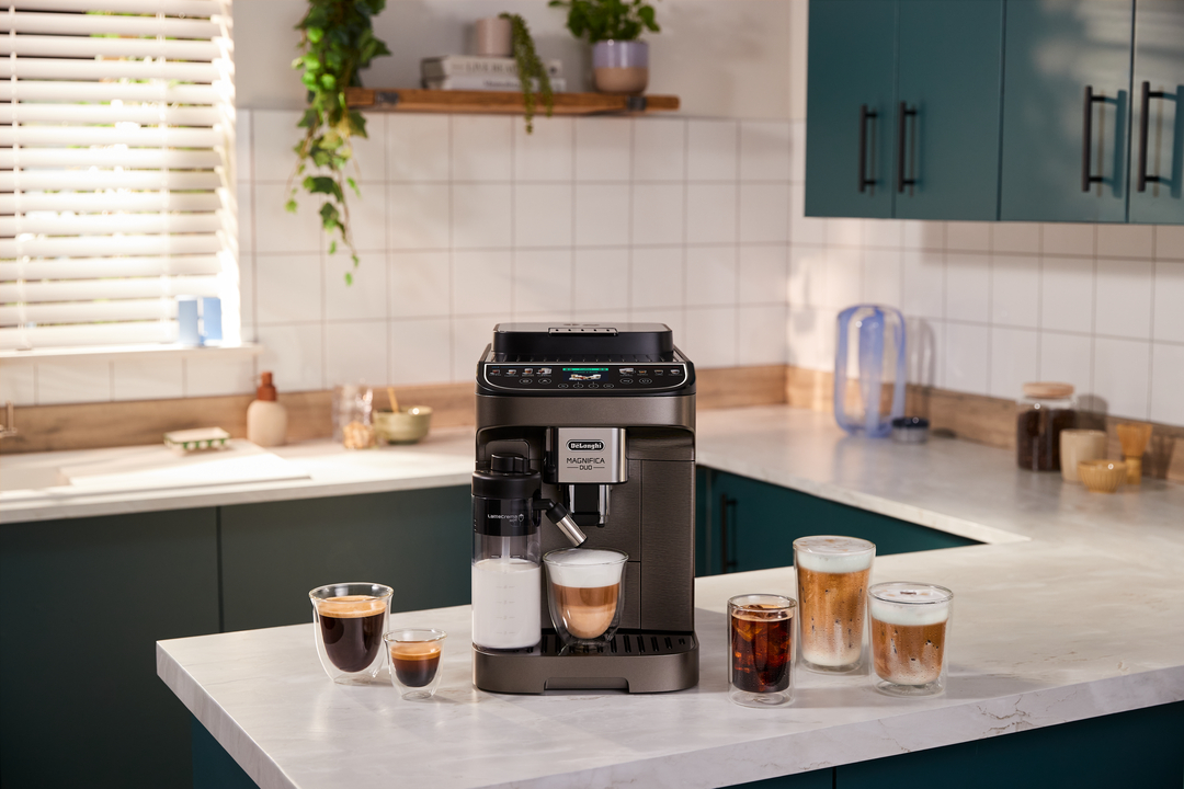 Una macchina da caffè DeLonghi Magnifica Duo grigio scuro su un bancone da cucina, con quattro bevande.