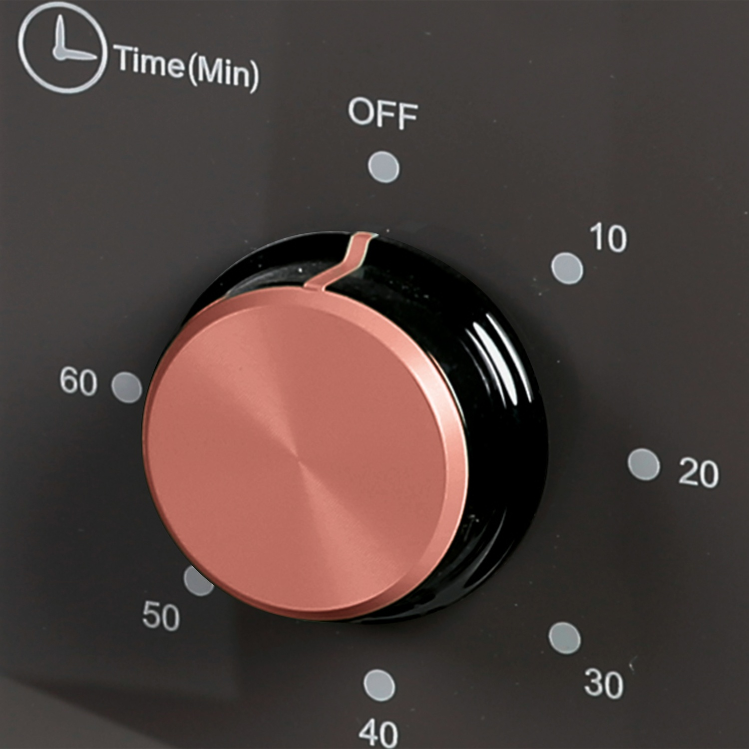 Una manopola del timer in oro rosa su un pannello di controllo scuro con segni di minuti.
