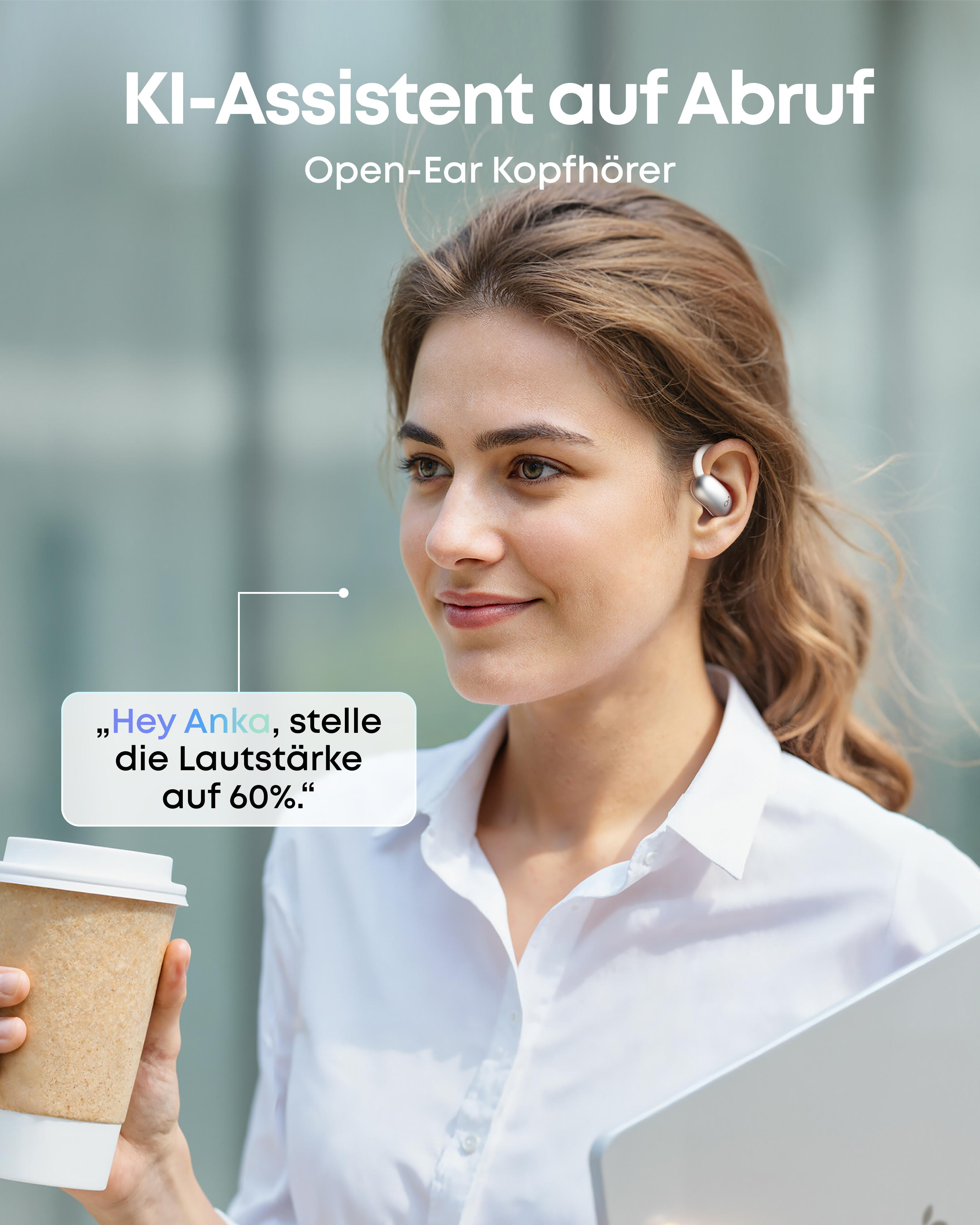 Frau mit Kopfhörern, Kaffeetasse und Laptop spricht mit KI-Assistent.