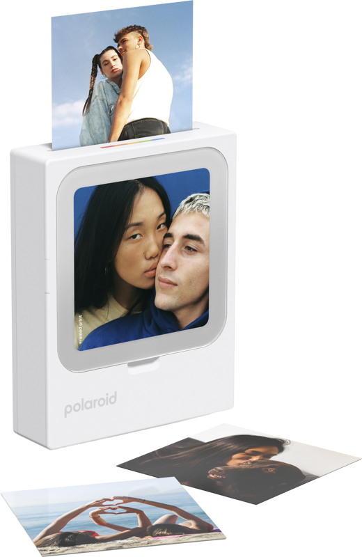 Biała drukarka Polaroid drukuje zdjęcie dwójki młodych ludzi, obok leżą kolejne wydrukowane zdjęcia.