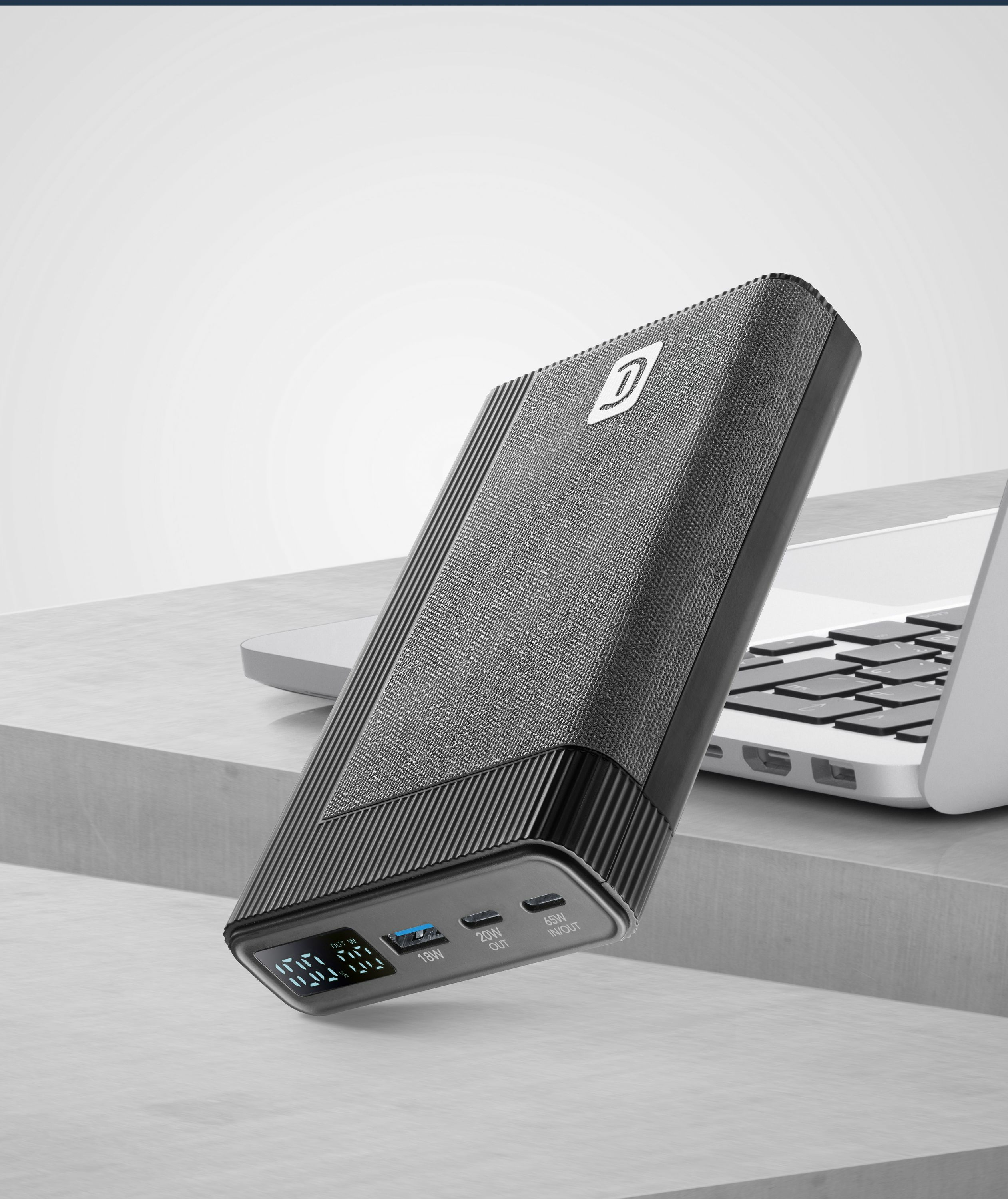 Un power bank negro con tela texturizada y logo junto a un portátil.
