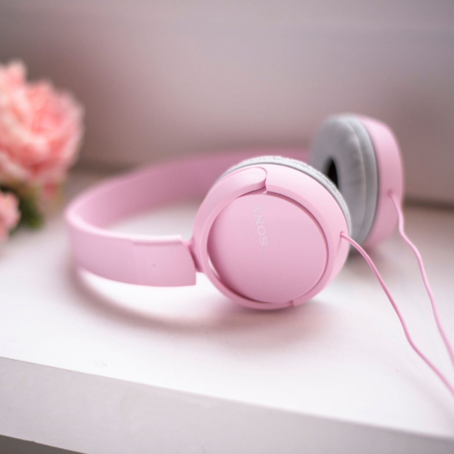 Unos auriculares Sony rosas descansan sobre una superficie blanca con flores cerca.