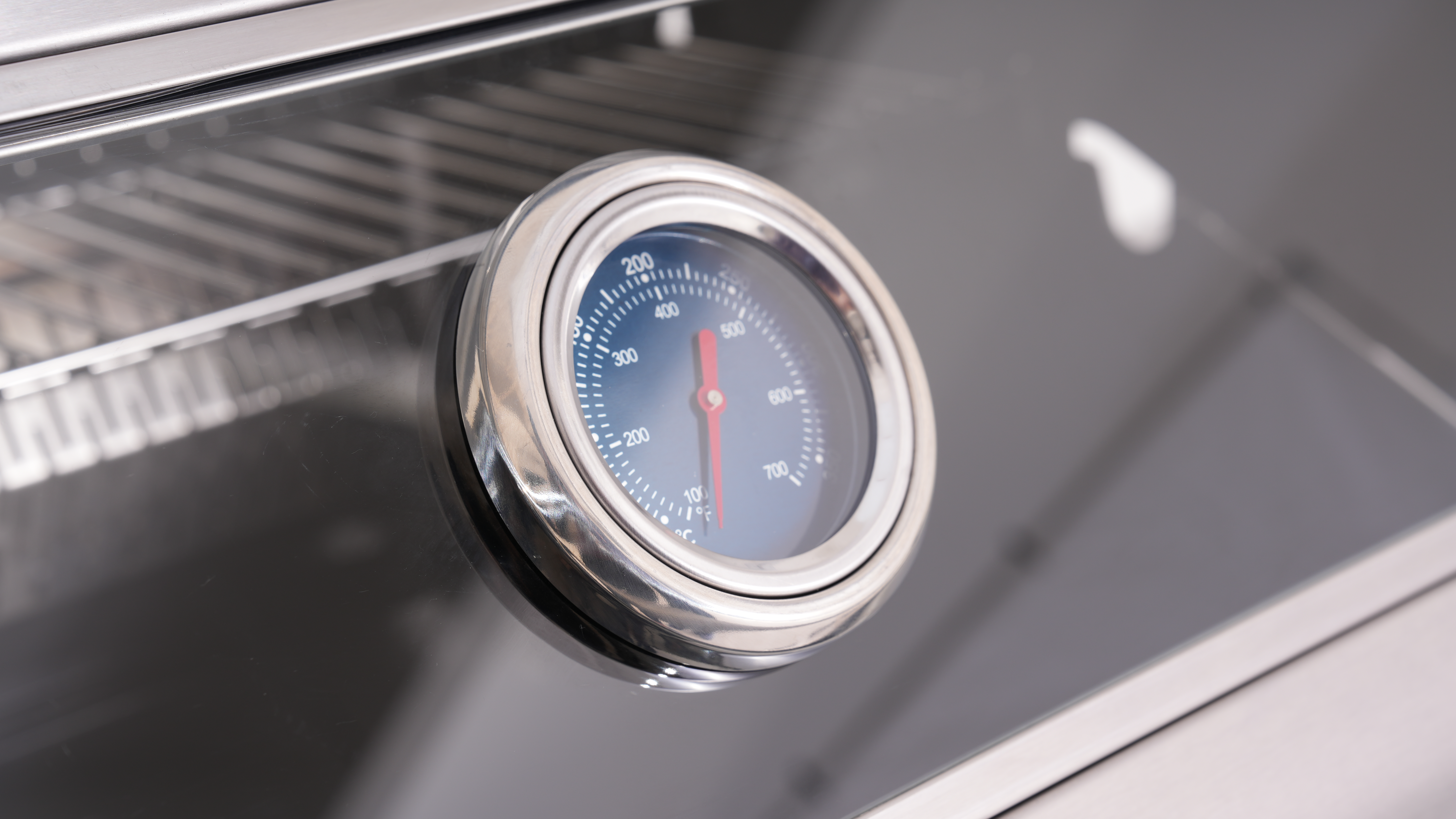 Ein Thermometer mit rotem Zeiger auf einem Grill, das 100°C anzeigt.