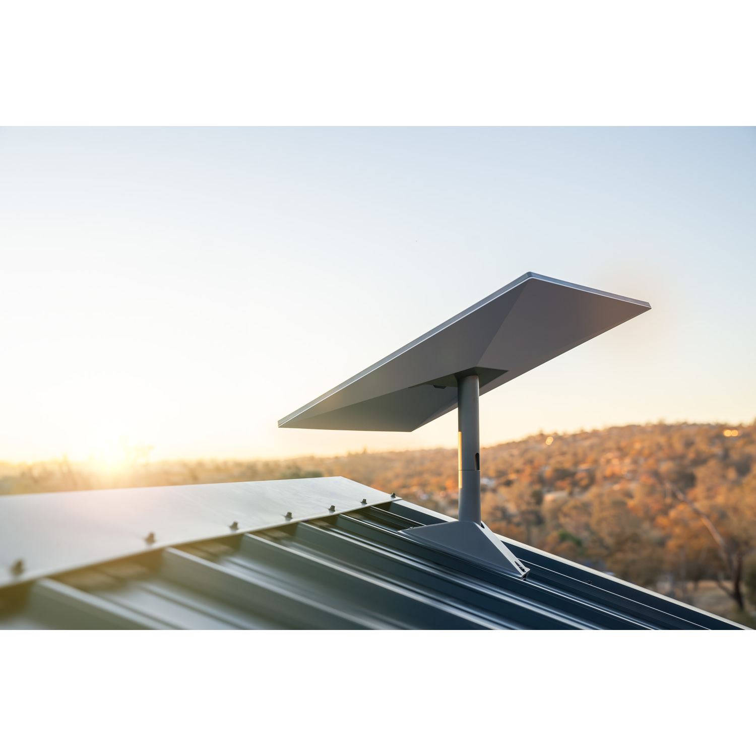 Een grijze schotelantenne op een metalen dak bij zonsondergang met heuvels op de achtergrond.