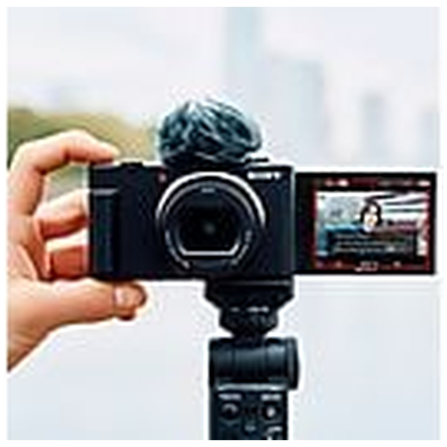 Une main tient un appareil photo Sony avec micro et écran rabattable.