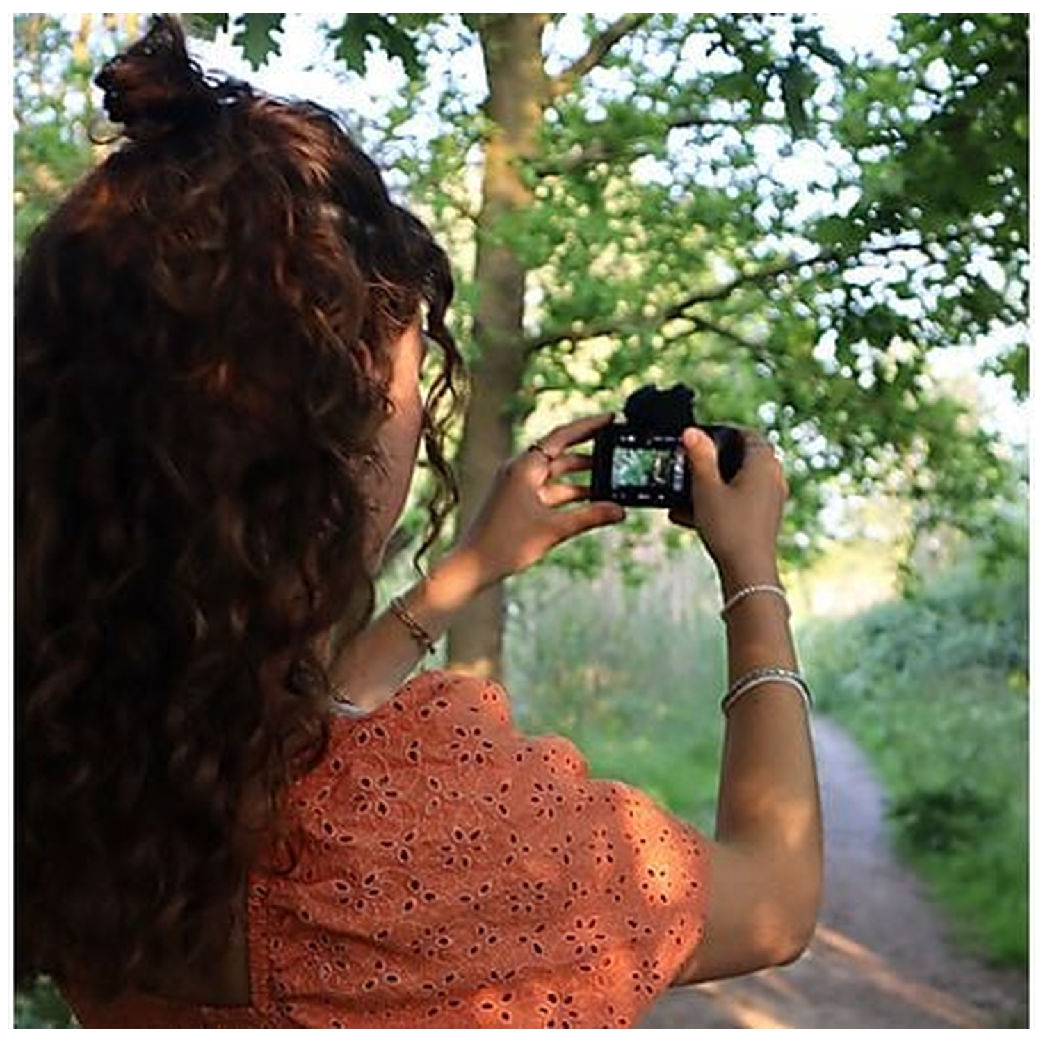 Femme aux cheveux bouclés prend photo avec appareil dans un sentier.