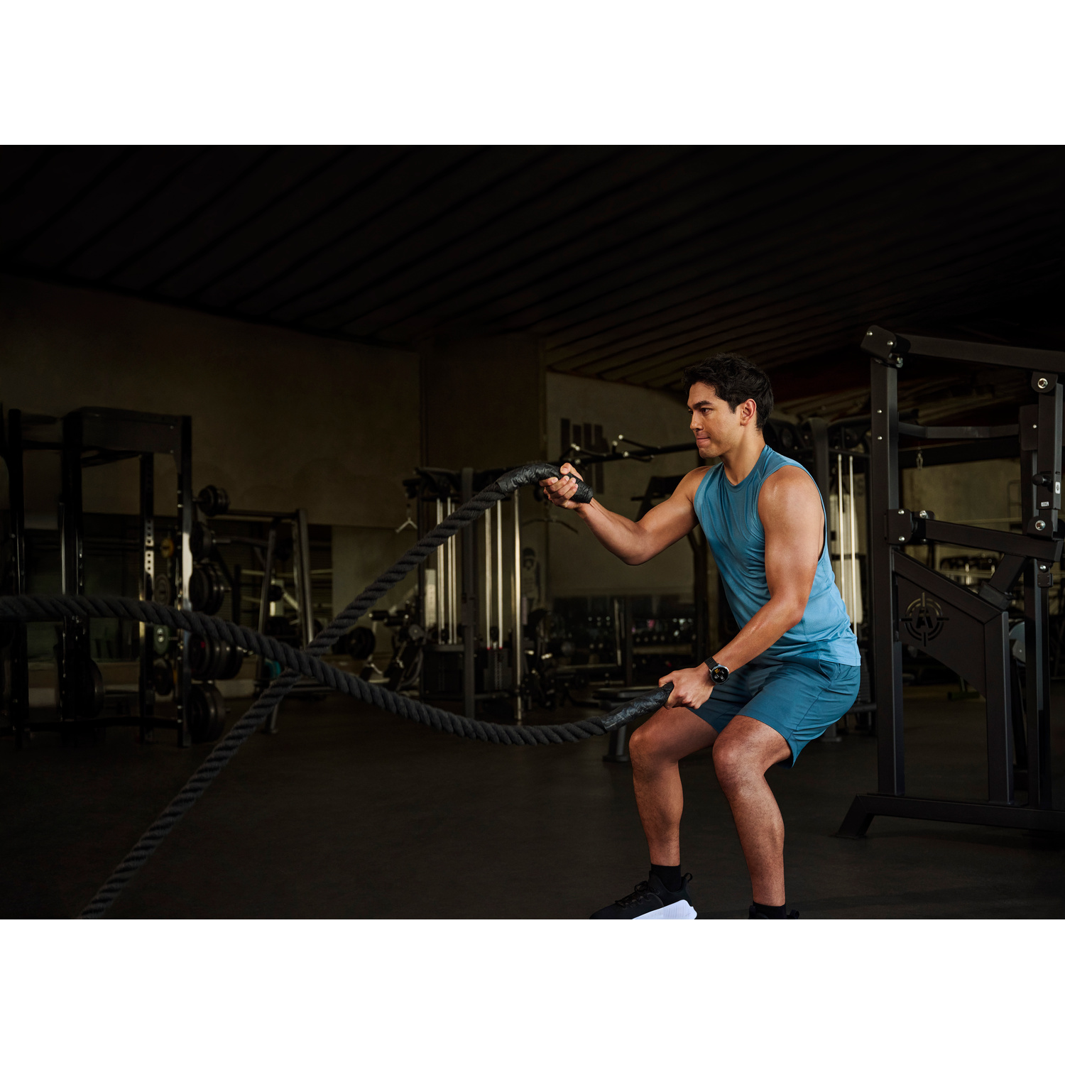 Un uomo in abbigliamento sportivo si allena con una fune pesante in una palestra.