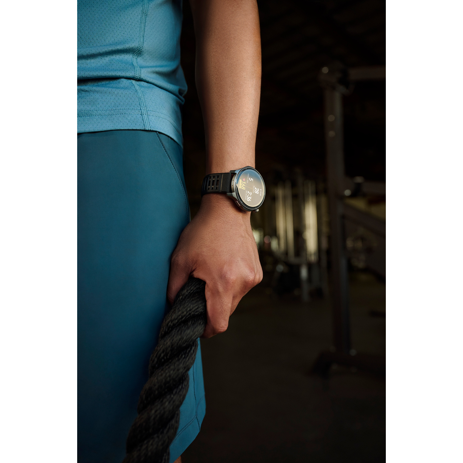 Un uomo afferra una fune spessa in una palestra, indossa un orologio sportivo.