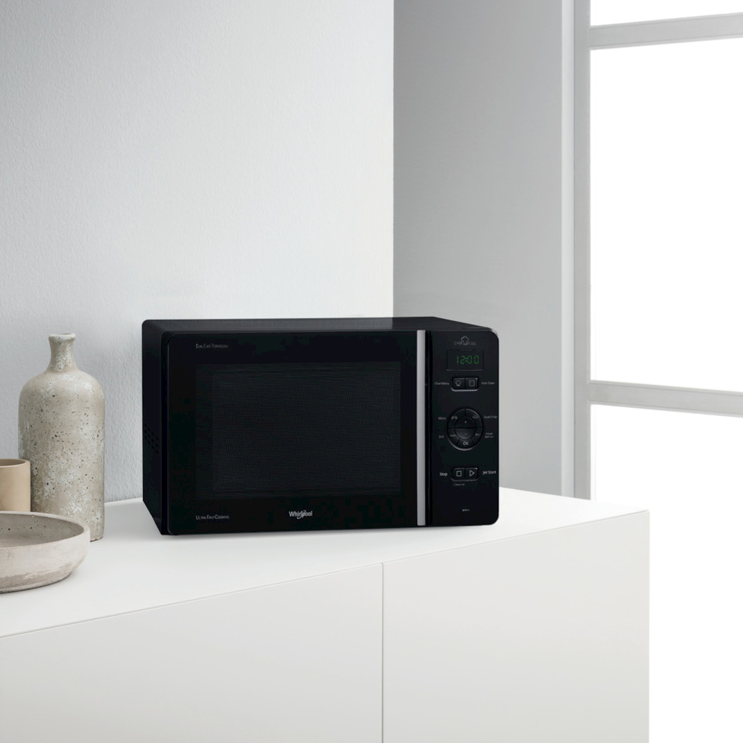 Un forno a microonde nero è su un mobile bianco accanto a vasi.