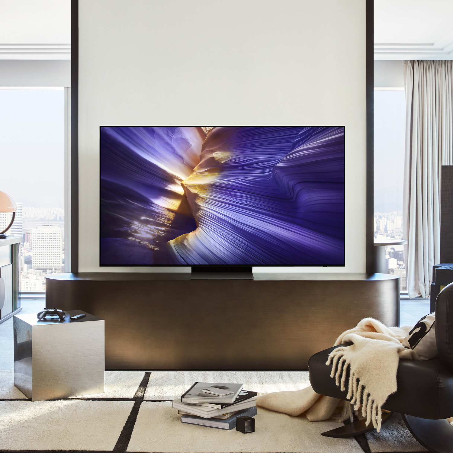 Soggiorno moderno con grande TV che mostra arte astratta, cubo metallico e poltrona con coperta.