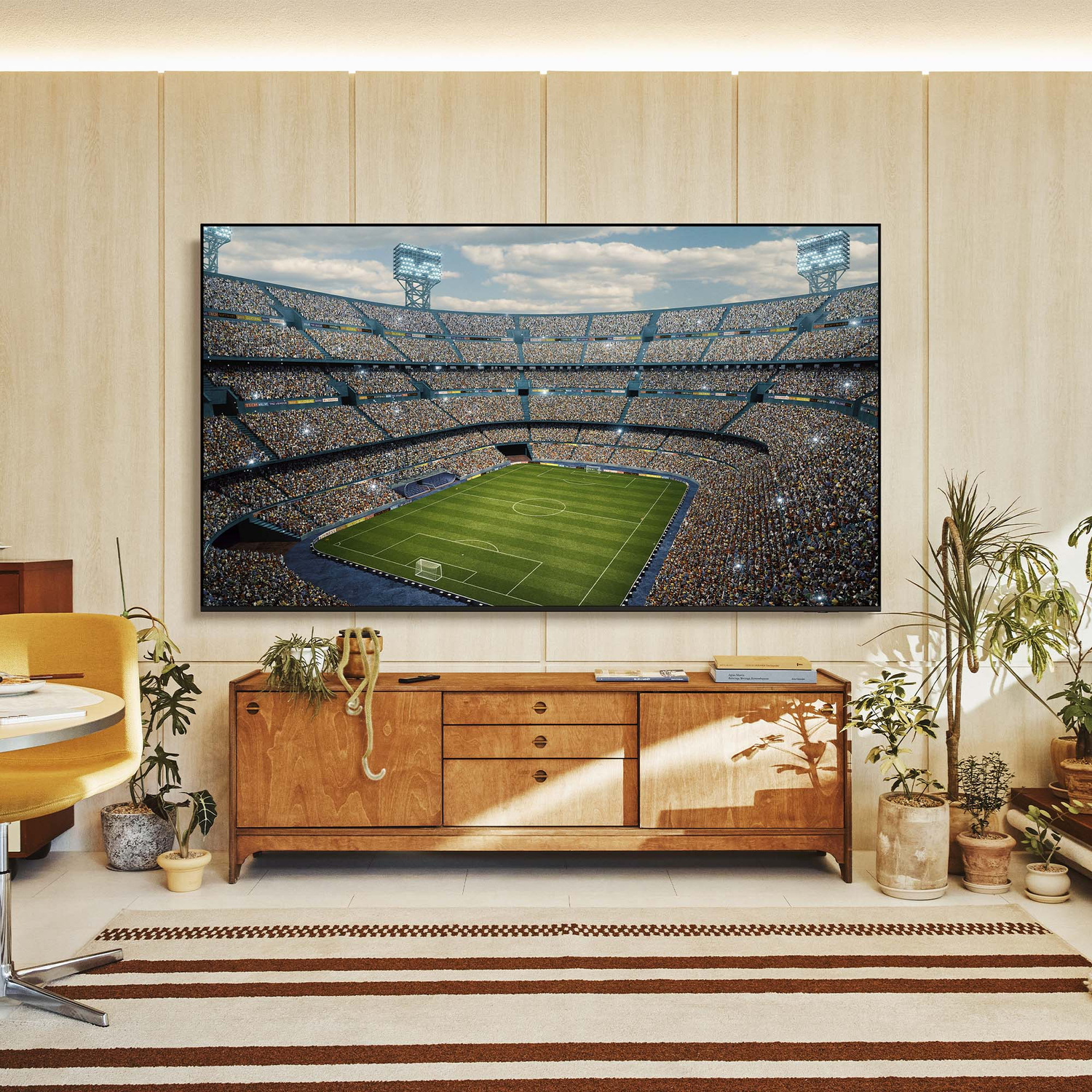 Una TV mostra uno stadio di calcio pieno di spettatori. Sotto c'è un mobile in legno.