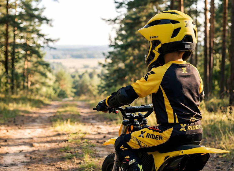 Dziecko w żółtym stroju motocyklowym na żółtym motocyklu w lesie.