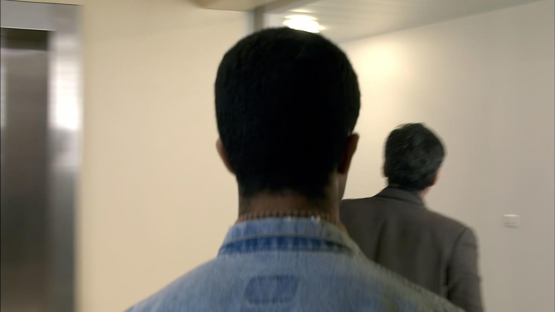 Zwei Männer gehen in einem Flur, einer in Jeans, der andere in einem Anzug.