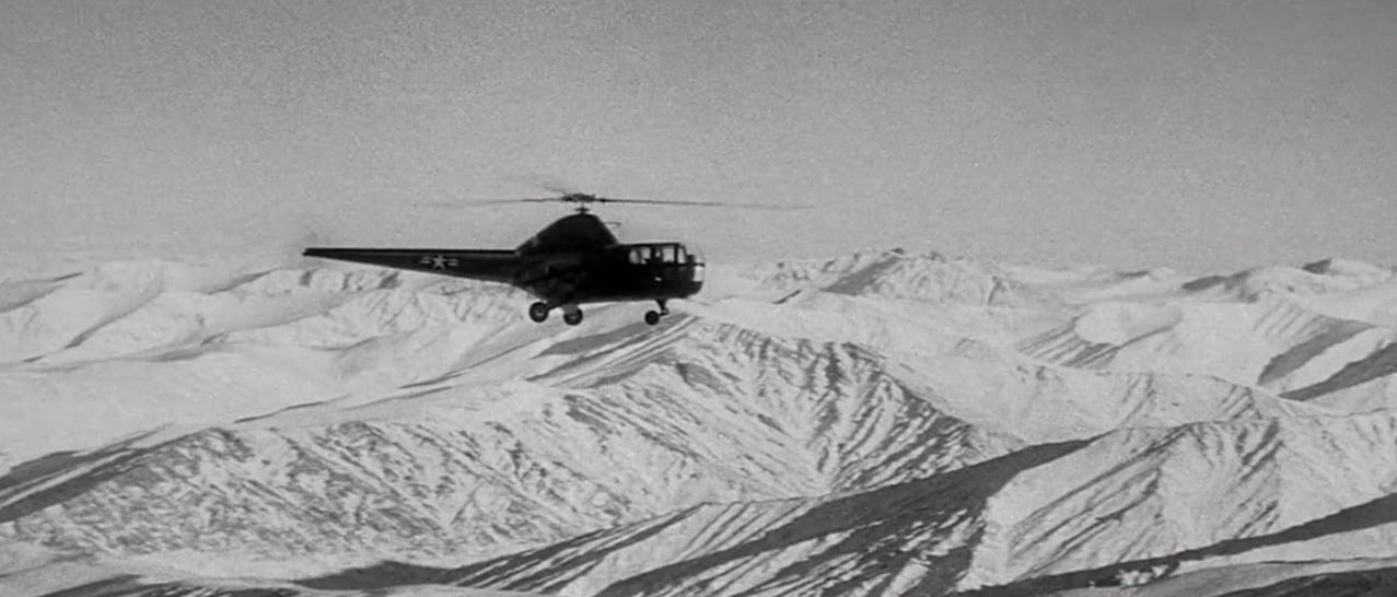 Ein Hubschrauber fliegt über schneebedeckte Berge.