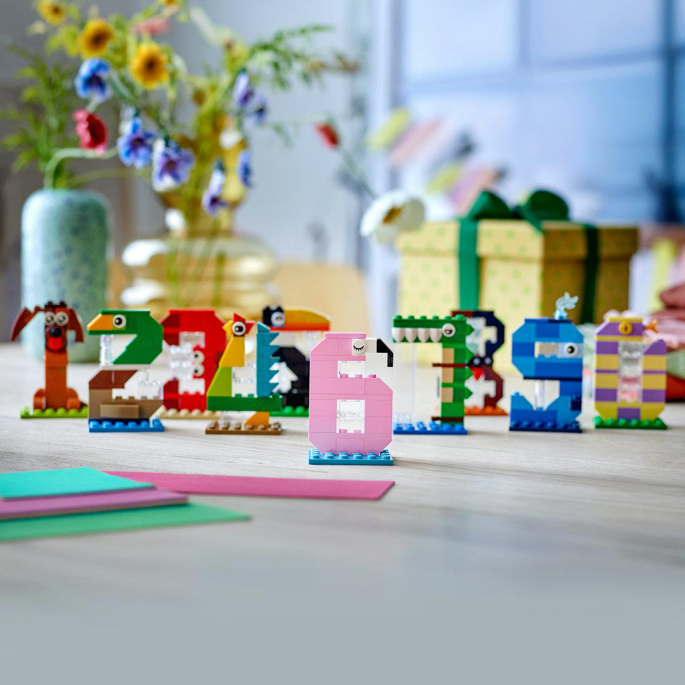 Lego-Zahlen 1-9 in Tierform. Im Hintergrund eine Geschenkbox und Blumen.