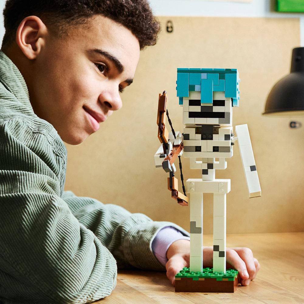 Junge betrachtet Lego Minecraft Skelett mit Bogen. Grüne Cordjacke.