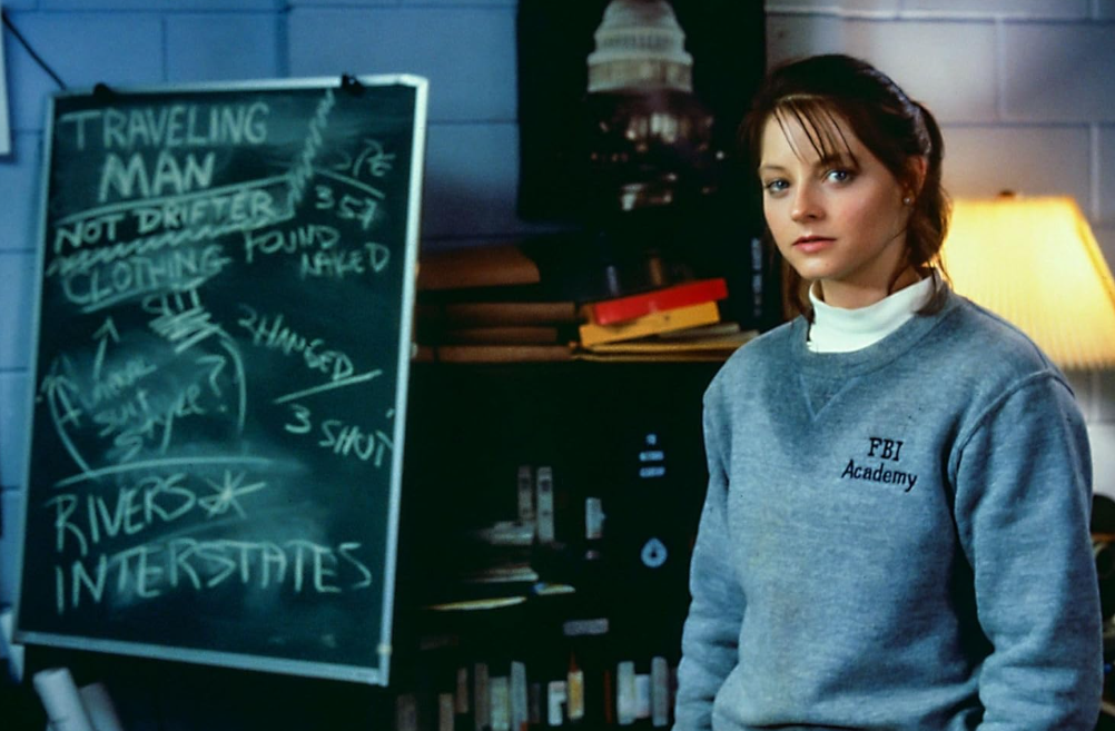 Eine Frau in einem grauen Sweatshirt mit FBI Academy-Aufdruck steht vor einer Tafel mit Notizen.