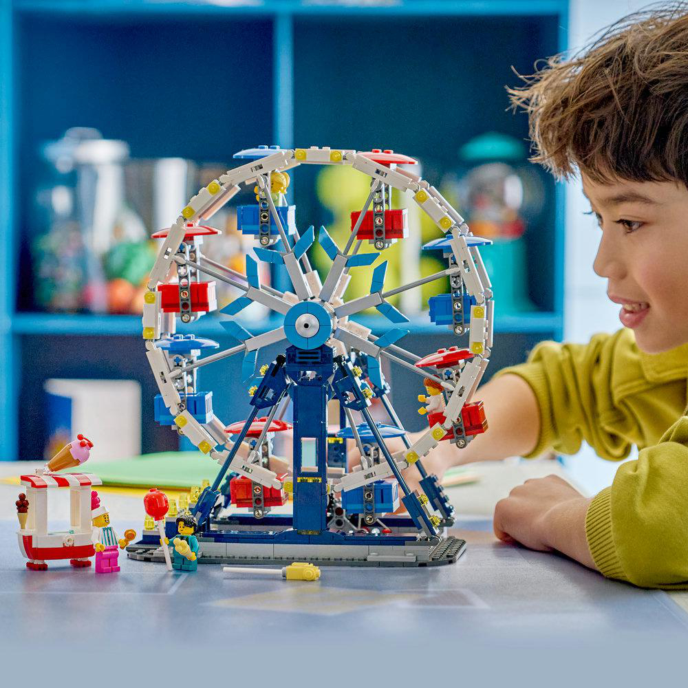 Ein Junge baut ein Lego-Riesenrad mit Eiswagen und Figuren. Dekorationen im Hintergrund.
