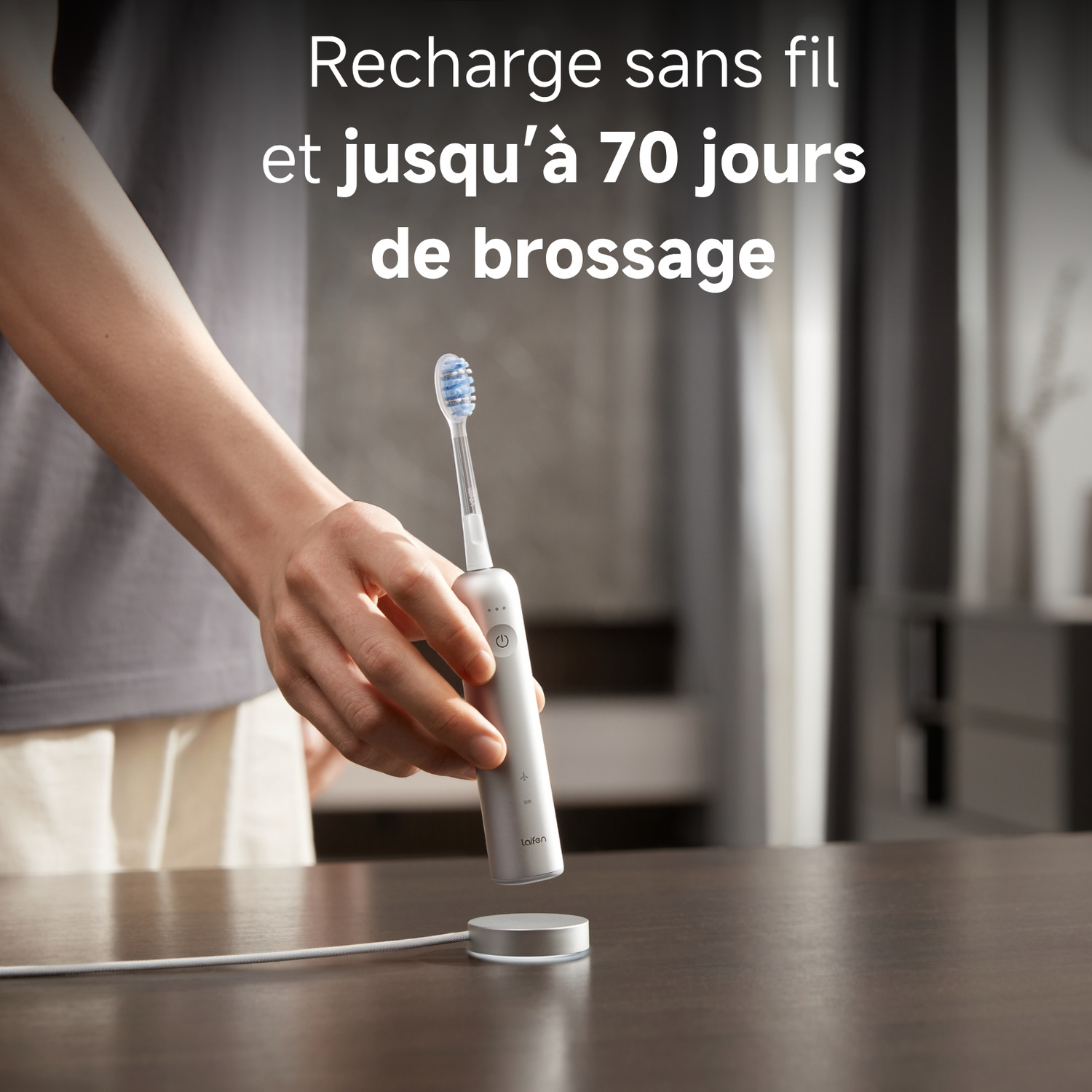 Une main tient une brosse à dents électrique argentée sur sa base de chargement.