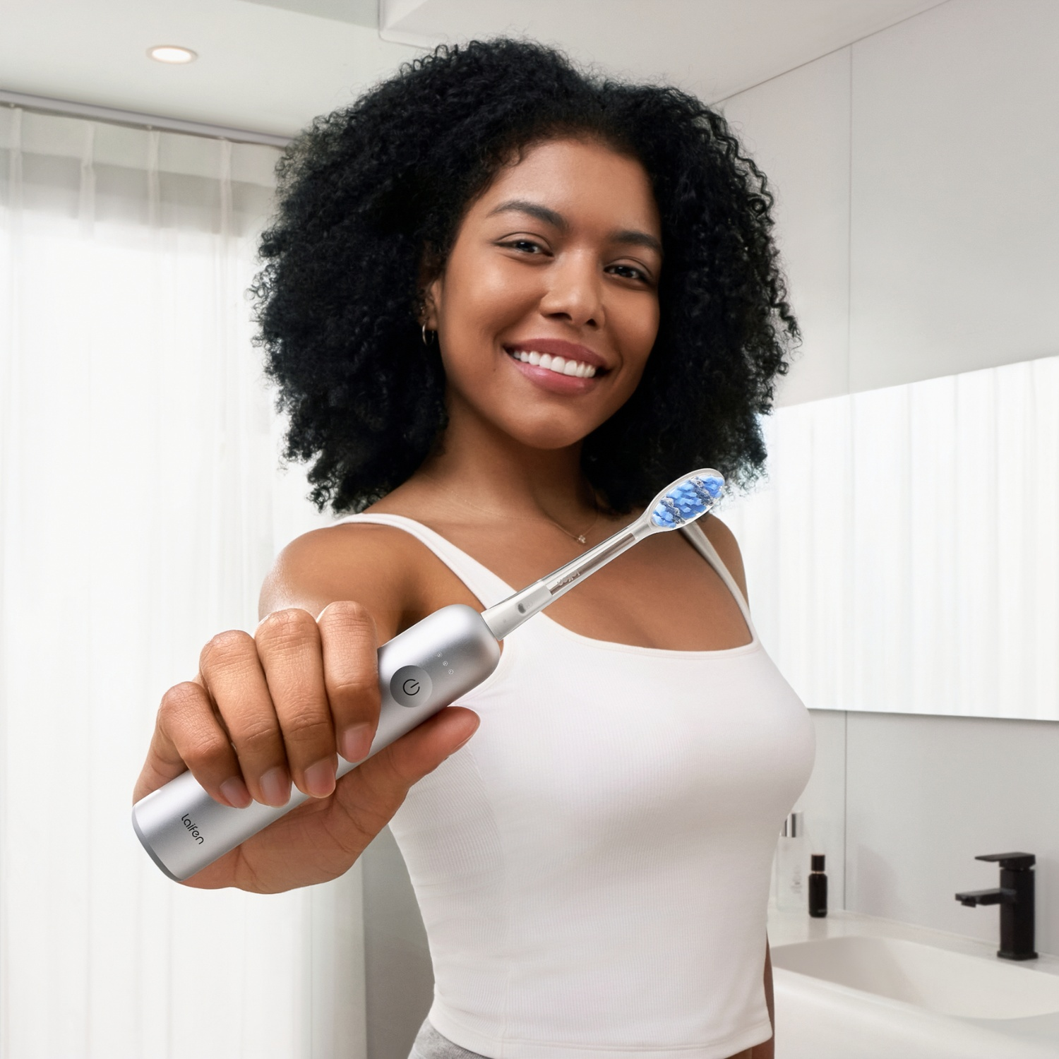 Femme tenant une brosse à dents électrique à poils bleus dans une salle de bain lumineuse.