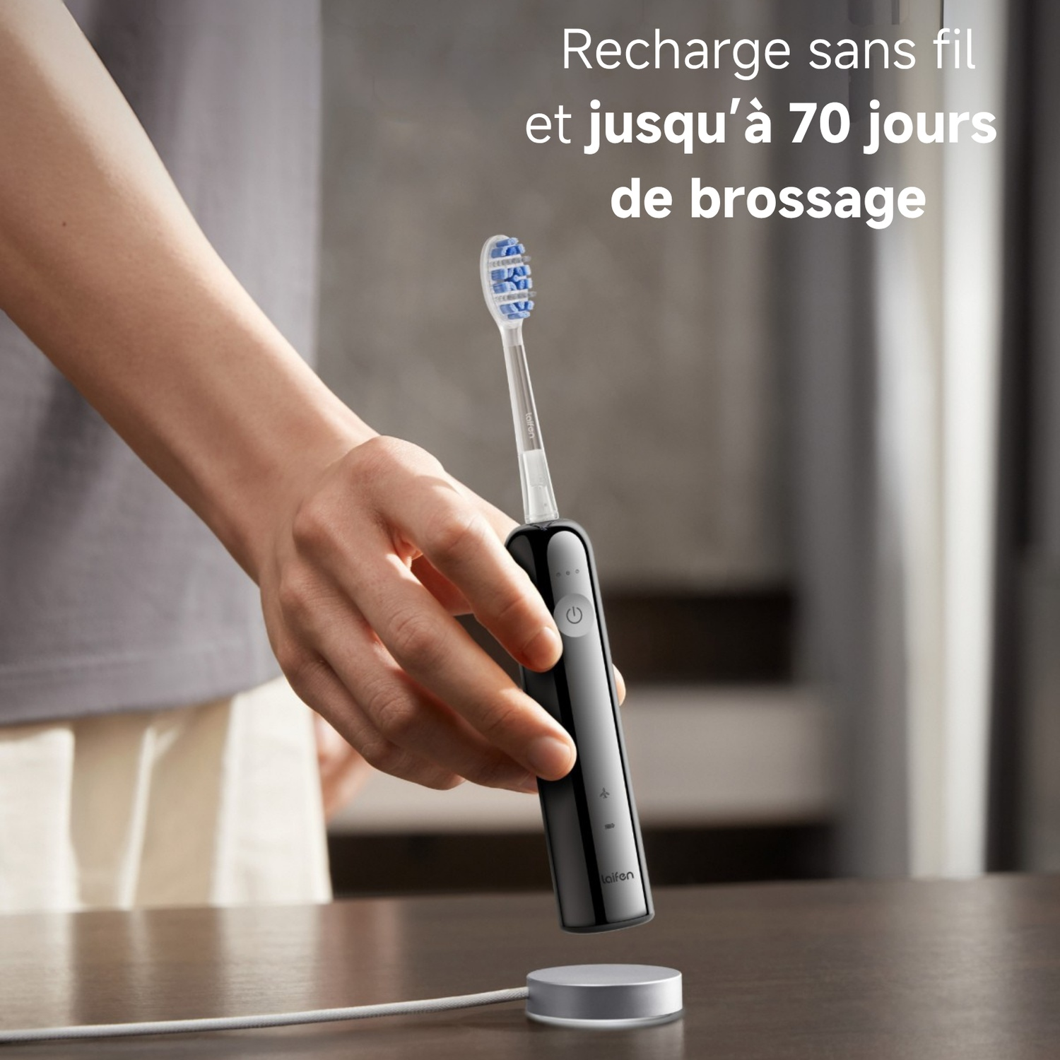 Une main tient une brosse à dents électrique noire sur une base de chargement.