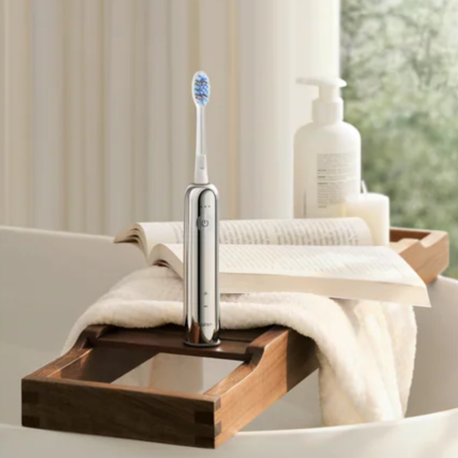 A silver electric toothbrush stands on a wooden tray in a bathtub, next to a book and soap.