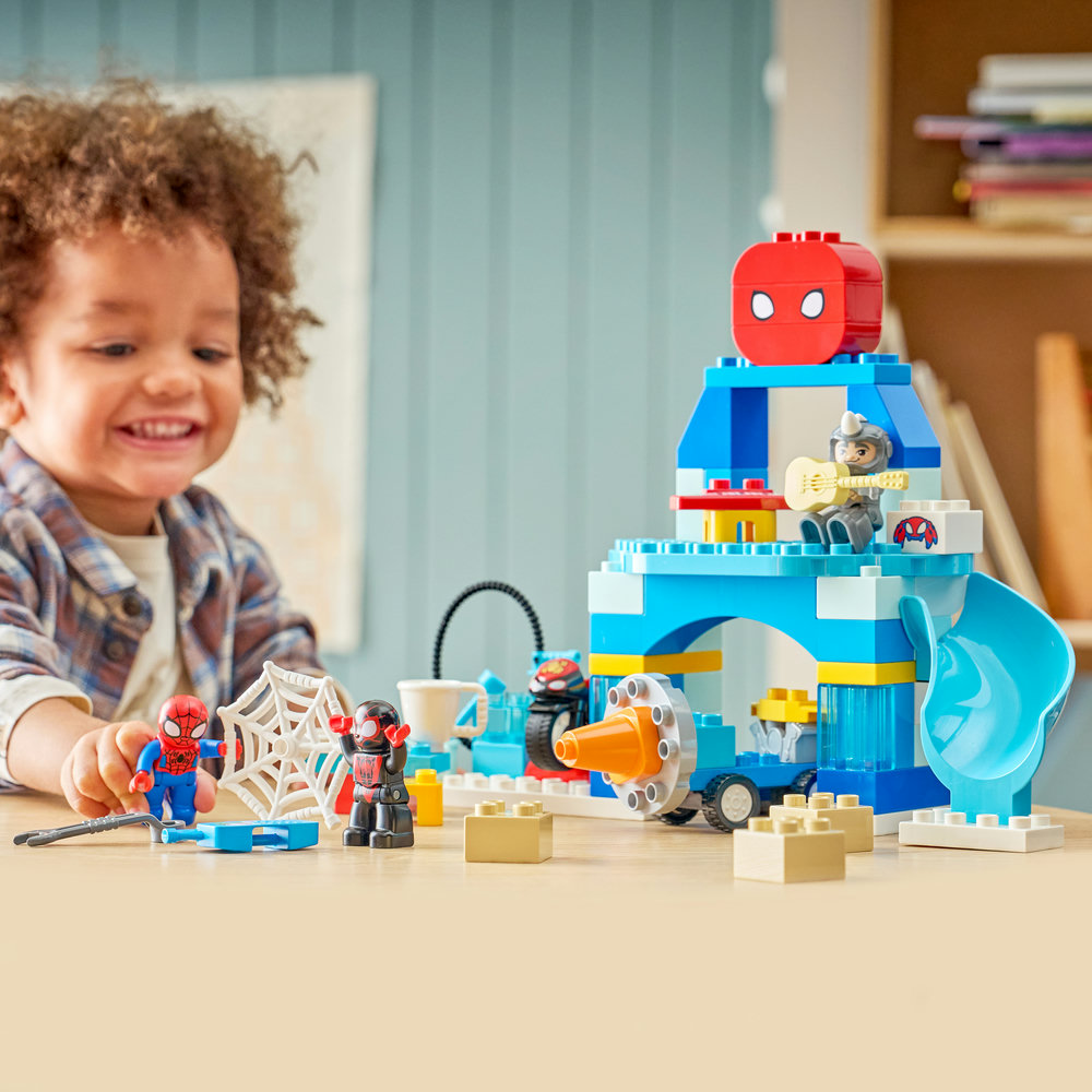 Ein Kind spielt mit Spiderman Lego auf einem Tisch, mit einem blauen und weißen Turm.