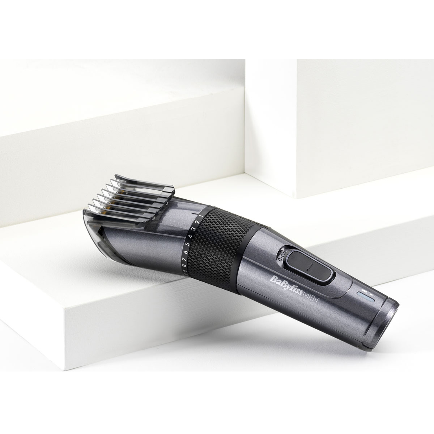 A gray hair clipper with a black grip rests on white steps.