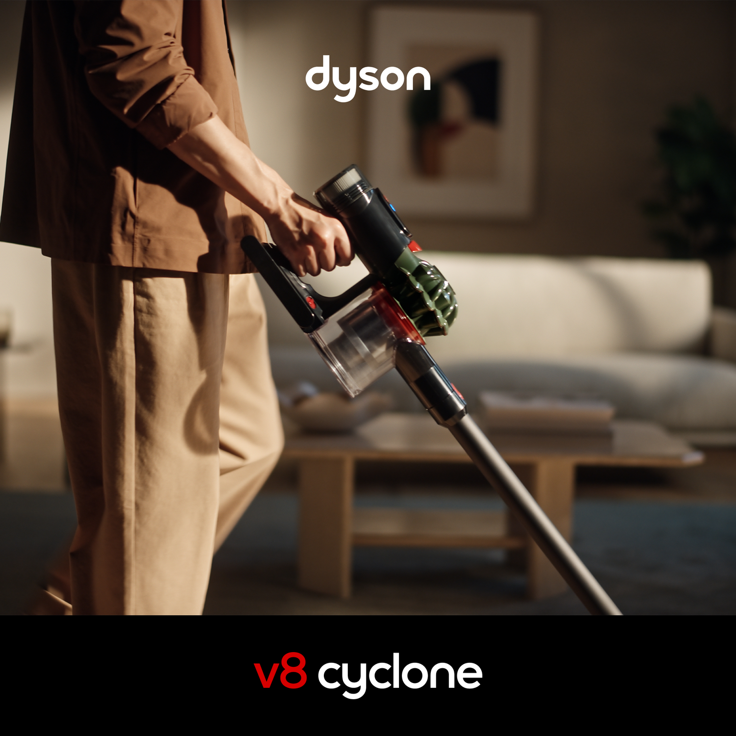 Persoon in bruine kleding houdt Dyson V8 Cyclone stofzuiger in woonkamer.
