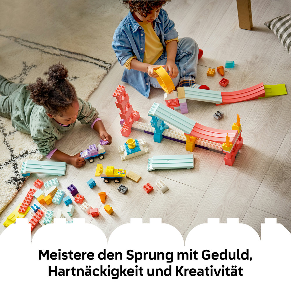 Zwei Kinder bauen mit bunten Bausteinen eine Rennstrecke auf dem Boden.