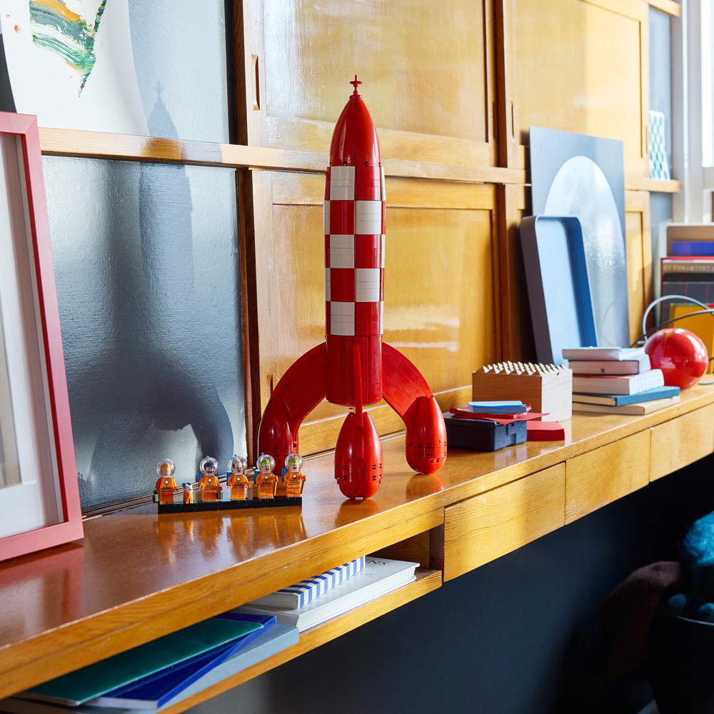 Ein roter Lego-Raketenbausatz mit weißen Karos auf einem Holzschreibtisch.