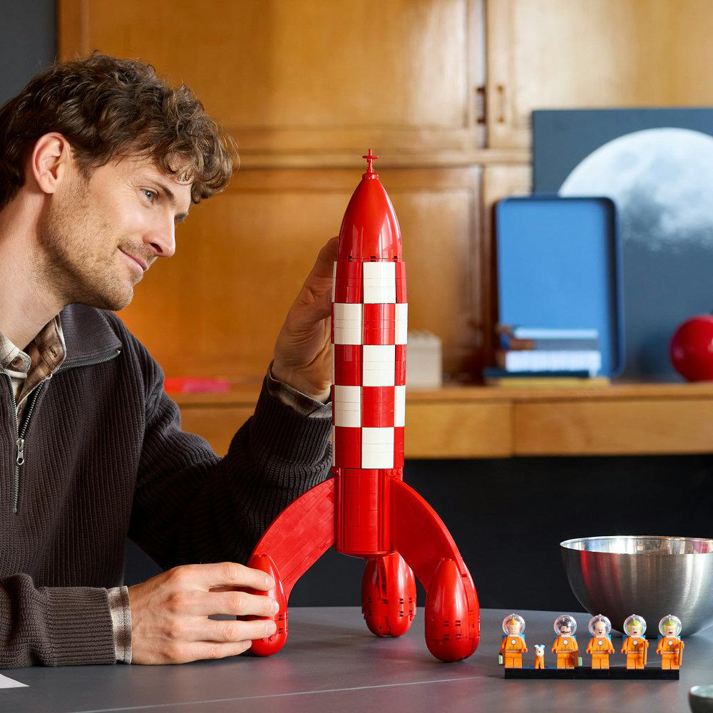 Ein Mann hält eine rote und weiße Rakete. Kleine Astronauten stehen daneben.
