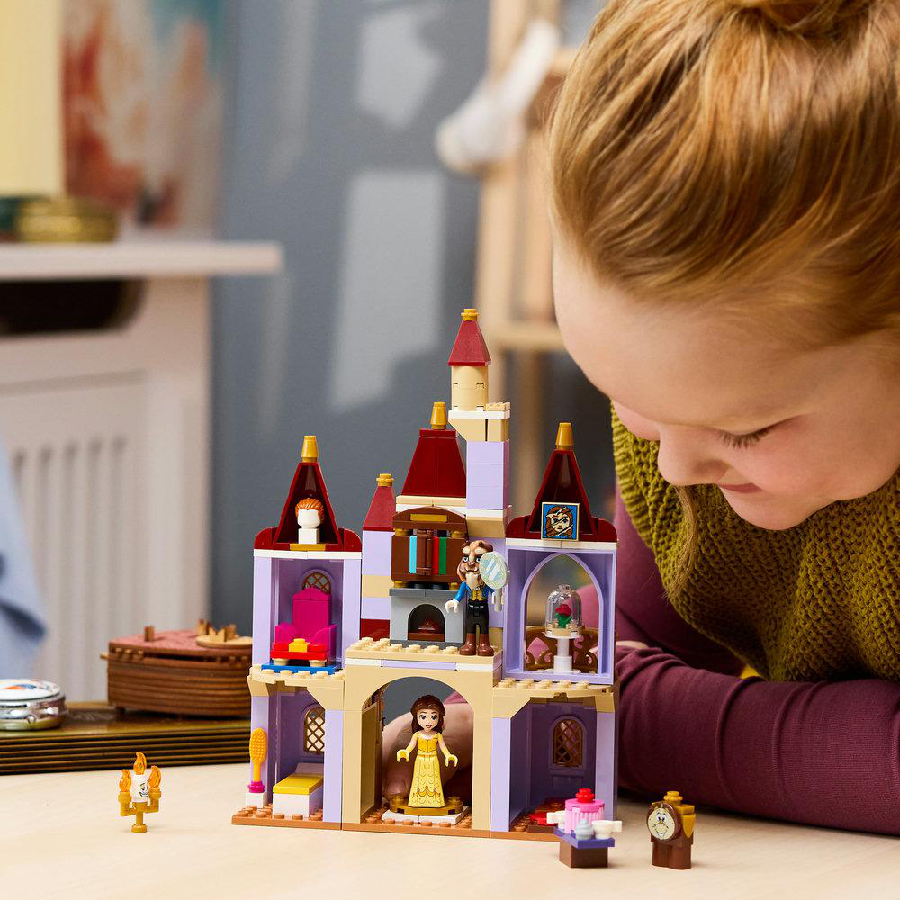 Ein Mädchen blickt auf ein Lego-Schloss mit Figuren, darunter Belle und das Biest.