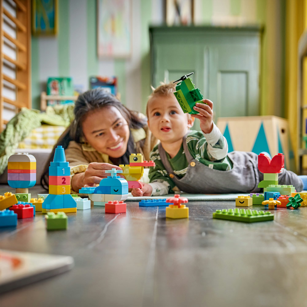 Mutter und Kind spielen mit bunten Duplo-Bausteinen auf dem Boden.