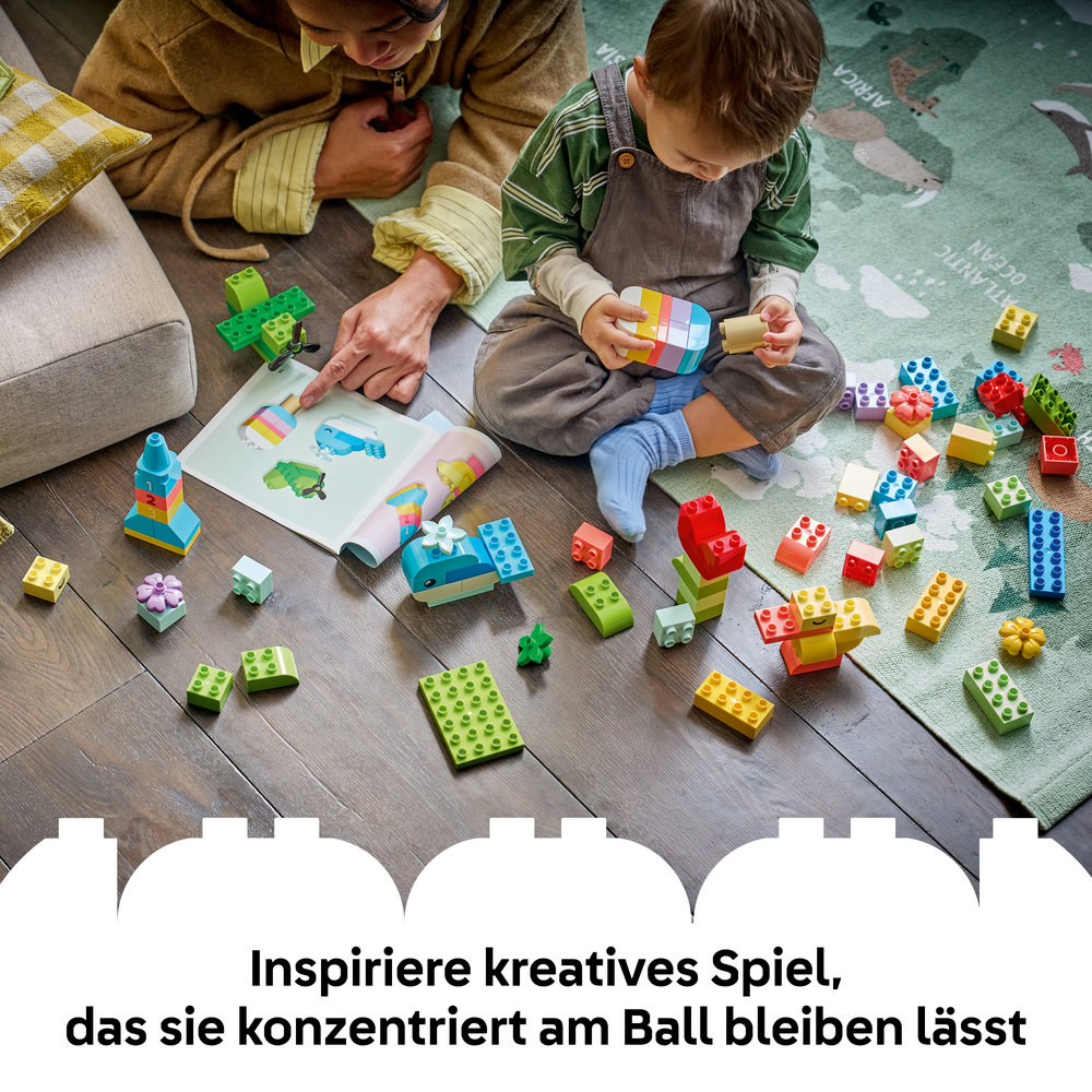 Erwachsene und Kind spielen mit bunten Bausteinen auf einem Teppich mit Weltkarte. Anleitung ist offen.