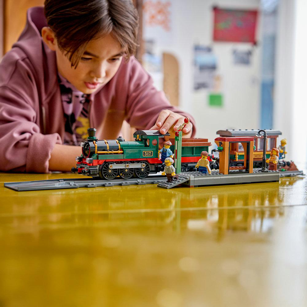 Junge spielt mit einem grünen Lego-Zug-Set an einem Bahnhof mit Figuren.
