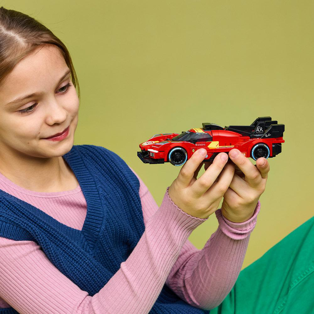 Ein Mädchen hält ein rotes Spielzeugauto mit schwarzen und gelben Akzenten. Der Hintergrund ist grün.