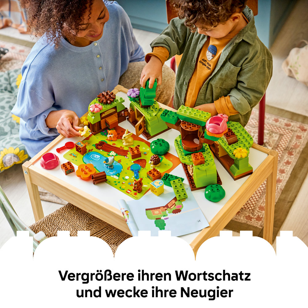 Frau und Kind bauen mit grünen Lego-Steinen an einem Tisch. Waldtiere sind auf der Spielmatte.