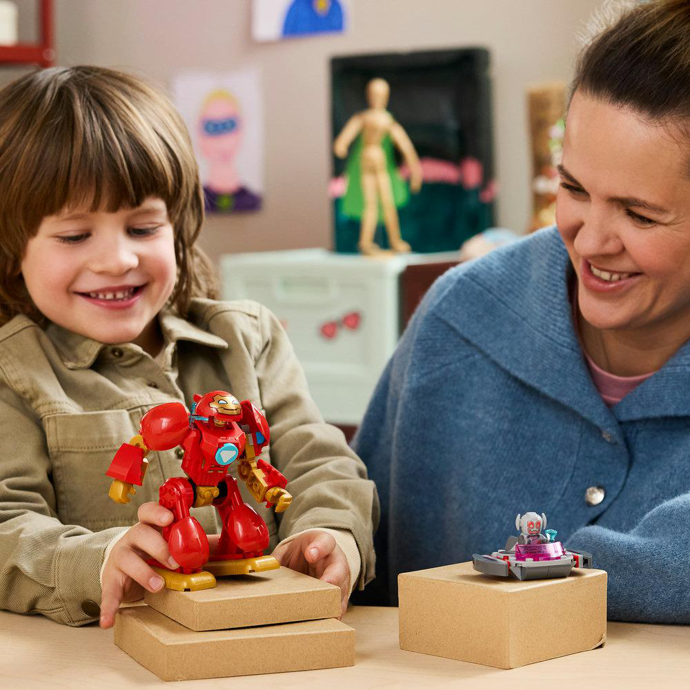 Ein lächelndes Kind hält eine rote Roboterfigur. Eine Frau lächelt daneben und schaut auf ein graues Spielzeugauto.