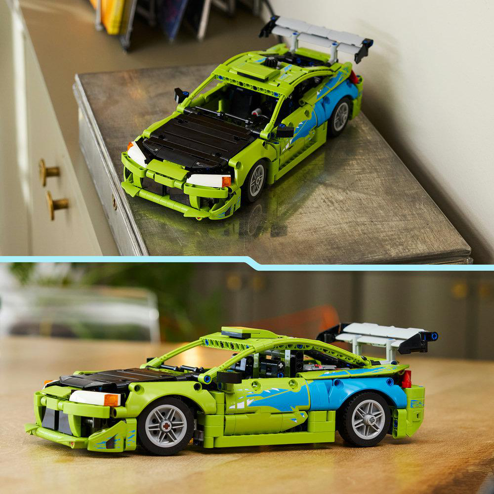 Grünes Spielzeugauto mit schwarzer Motorhaube und Spoiler auf Tisch und Holzhintergrund.