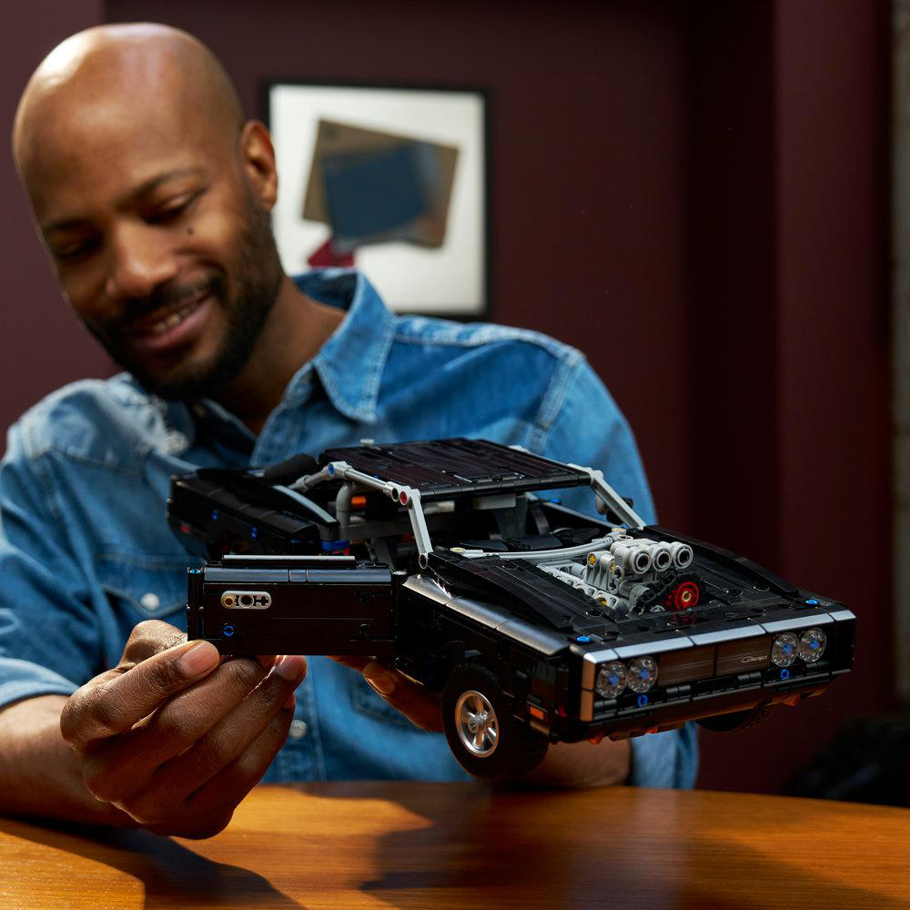 Mann hält ein schwarzes Lego-Automodell mit offener Tür und sichtbarem Motor.