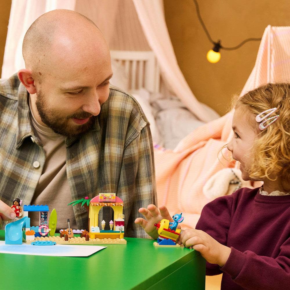 Mann und Kind bauen Lego am grünen Tisch. Strand-Thema mit Eisdiele und Rutsche.