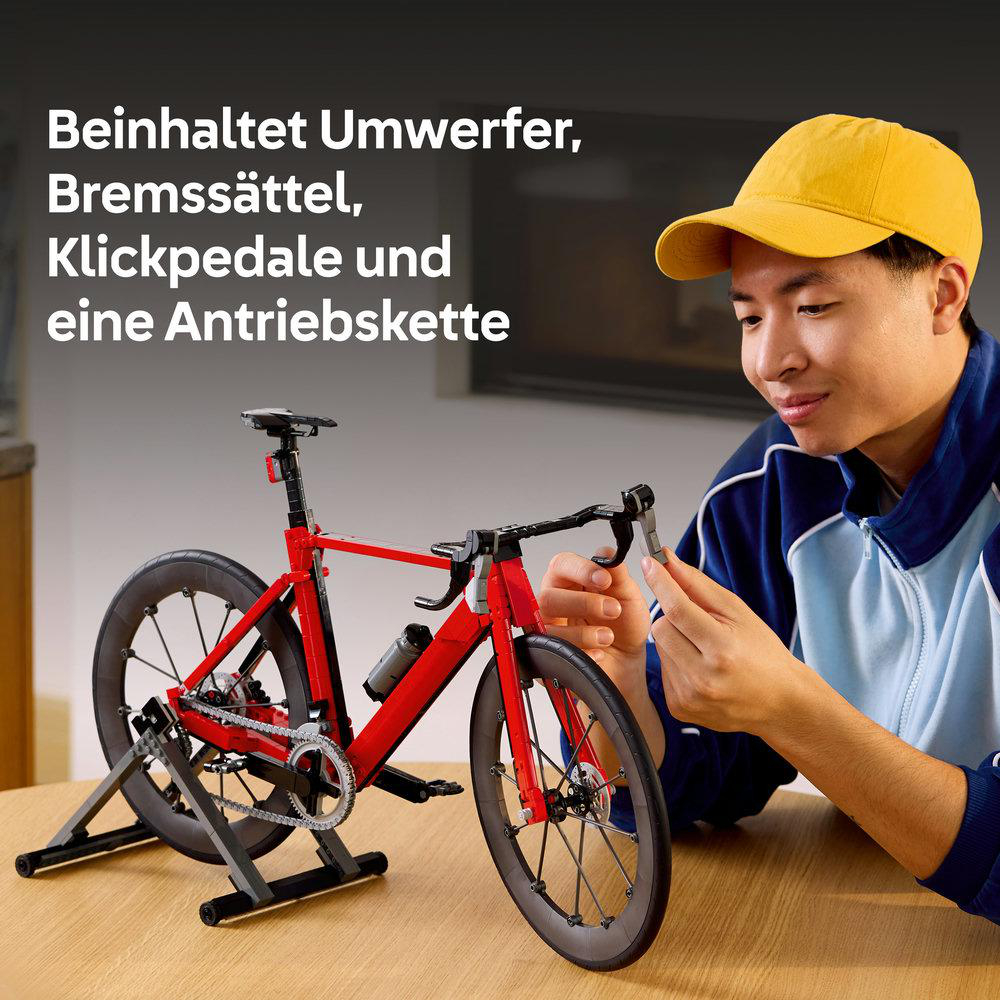 Ein Mann in einem gelben Hut baut ein rotes Modellfahrrad auf einem Holztisch.