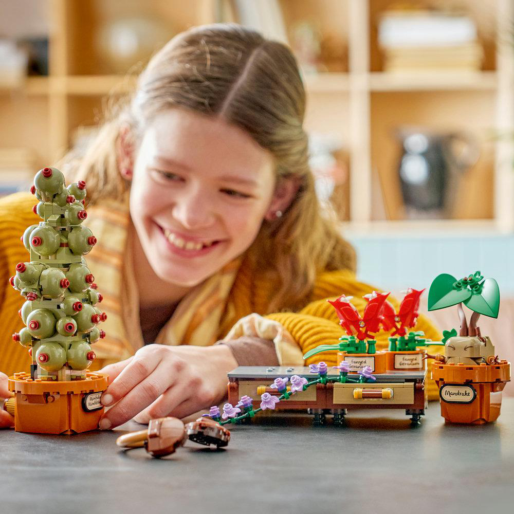 Ein Mädchen lächelt, während es mit Lego-Pflanzen spielt: ein Kaktus, eine Mandragora und rote Blumen.