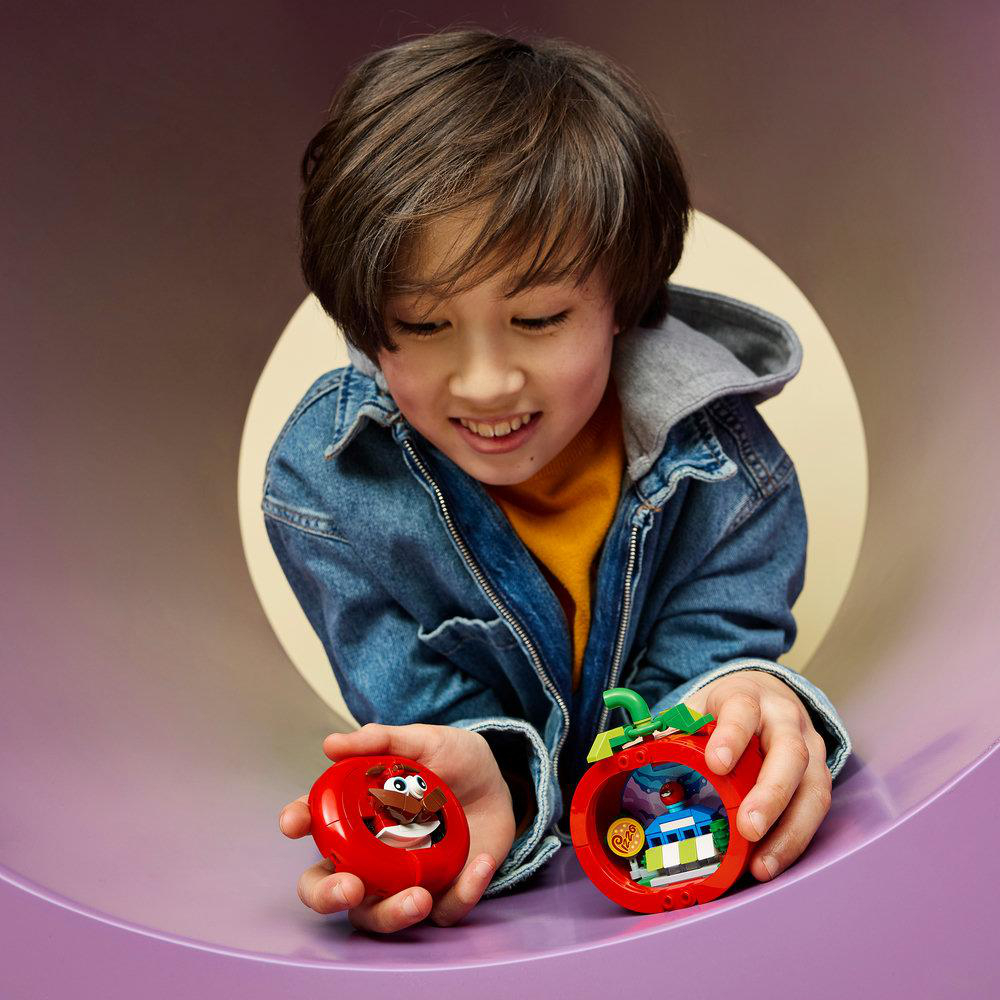 Ein Junge in Jeansjacke spielt mit roten Lego-Bausteinen in Form von Obst.