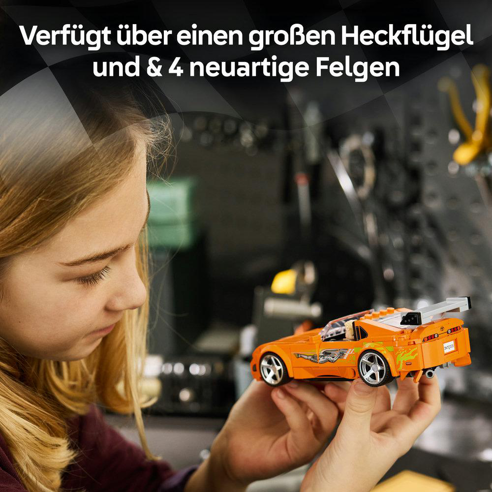 Mädchen hält ein orangefarbenes Lego-Auto mit großem Heckflügel und Felgen.