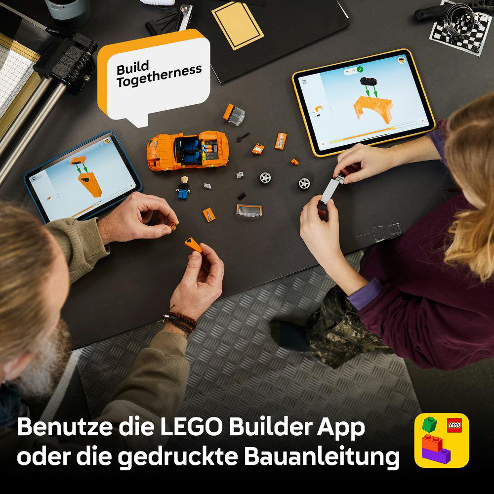 Zwei Personen bauen mit LEGO-Steinen. Tablets zeigen Bauanleitungen. Ein orangefarbenes Auto ist zu sehen.